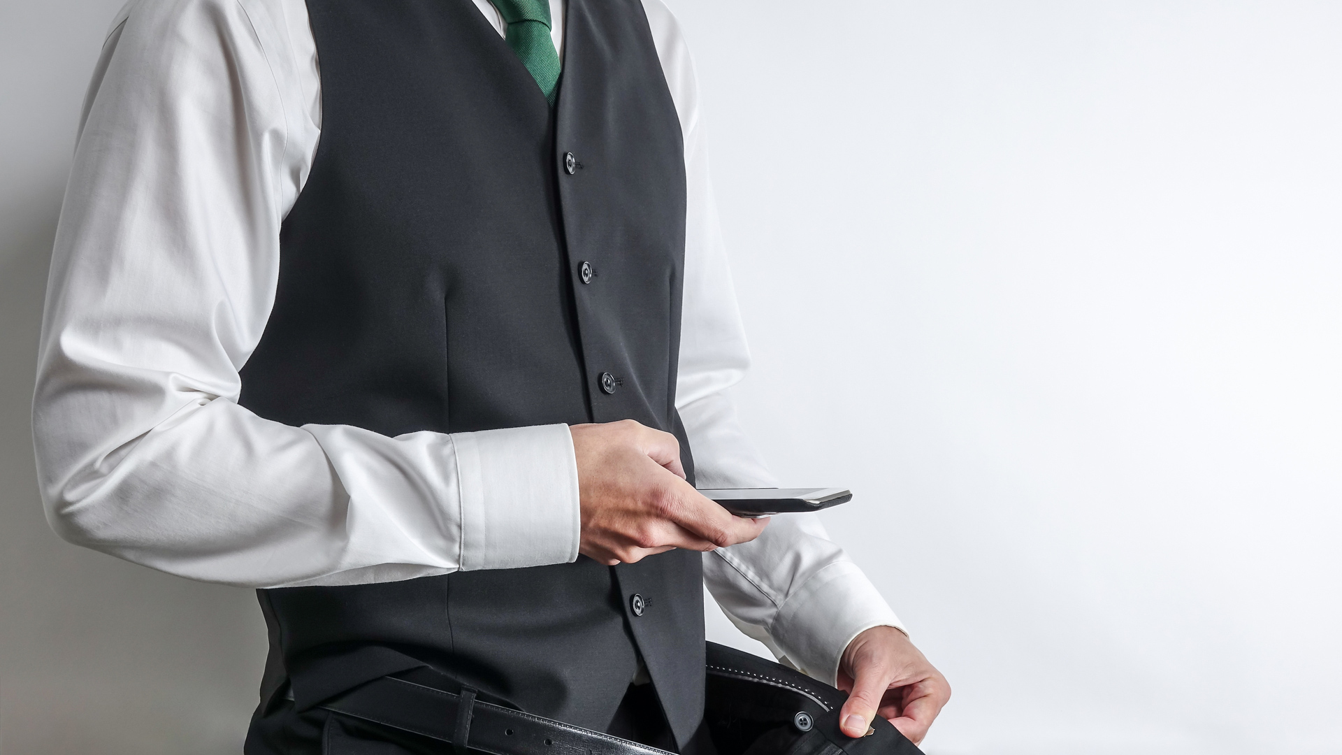 Man in a suit with green tie, holding his trousers open and his phone towards his crotch taking a picture.