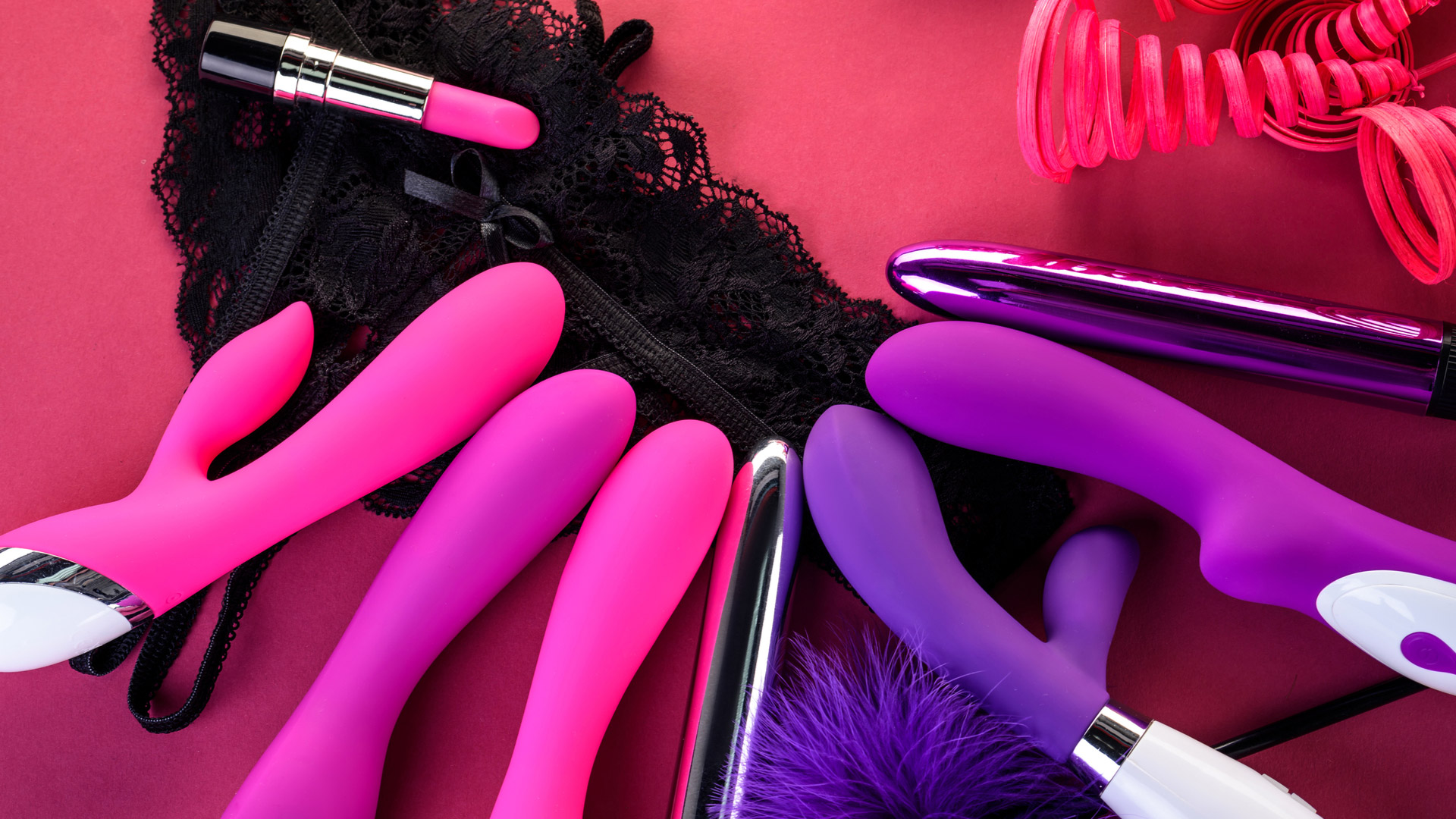 Multiple sex toys and pink lipstick lying in a circular position on black lingerie.
