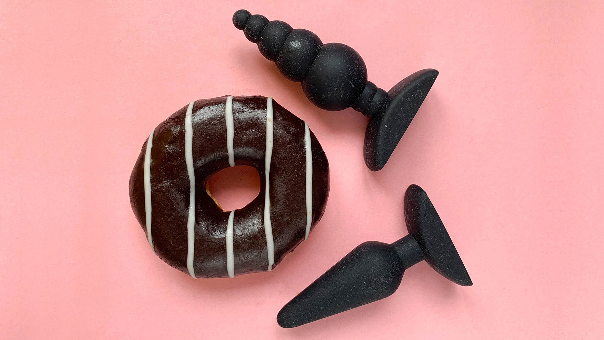 Two butt plugs with a with a black and white donut on a pink background.