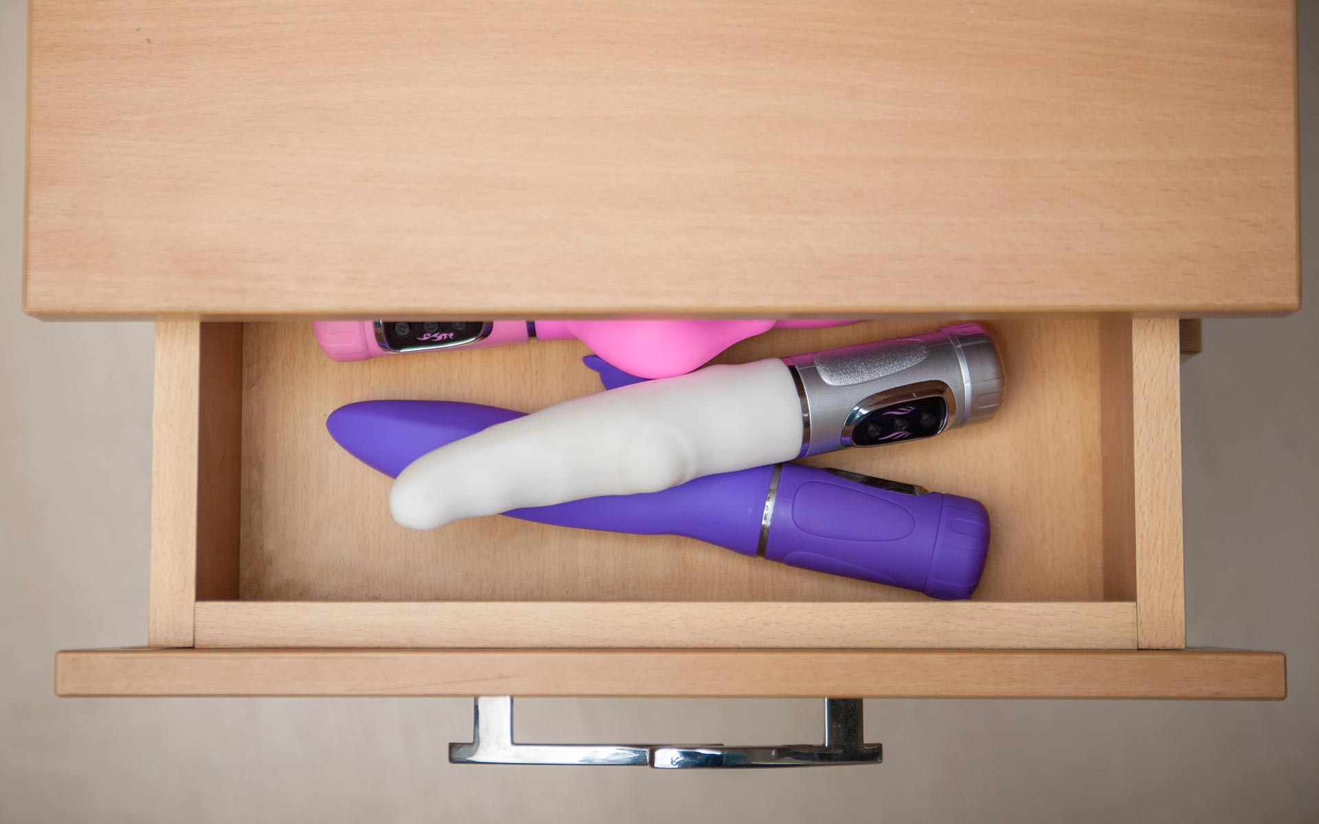 Light-brown wooden drawer furniture viewed from the top. The top drawer is open and contains many adult toys.