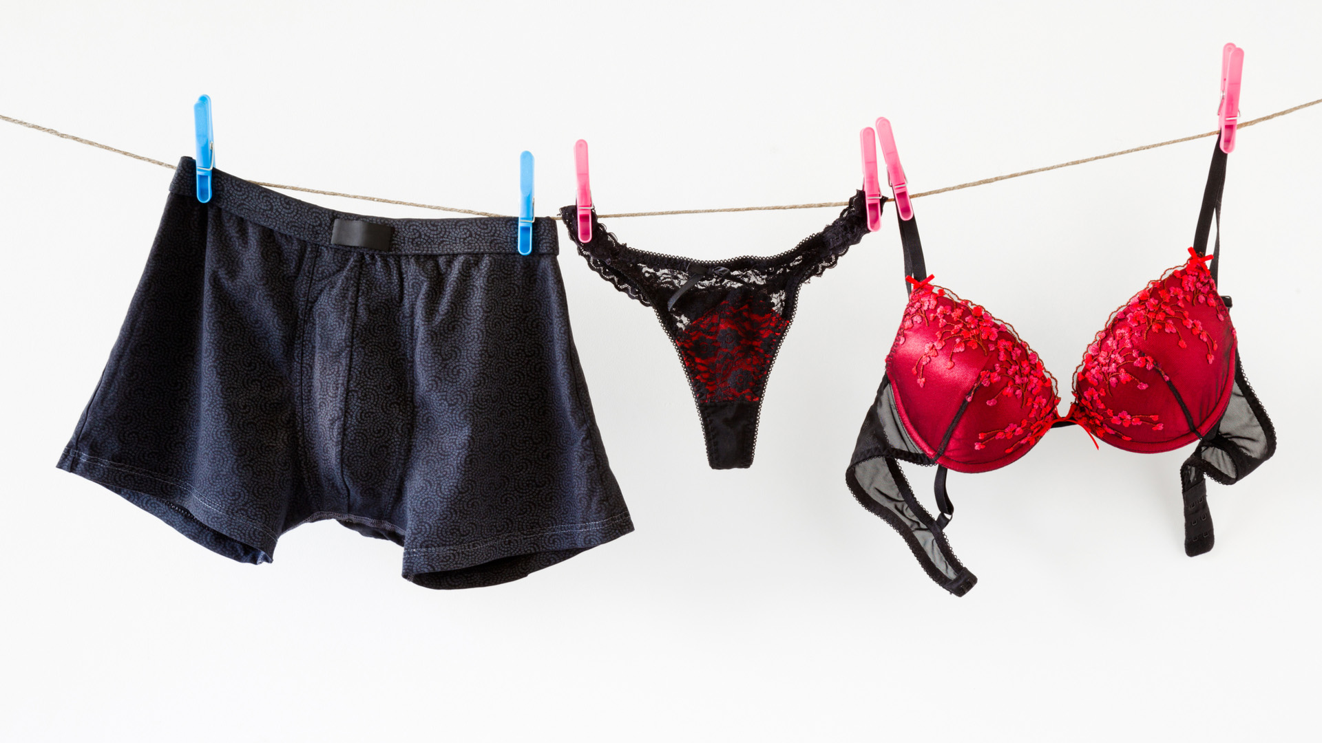 Navy boxer briefs next to black and red panties and bra hanging on a string.